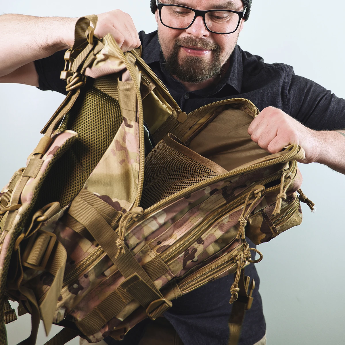 A man examining the compartments of a tactical backpack in camouflage design.
